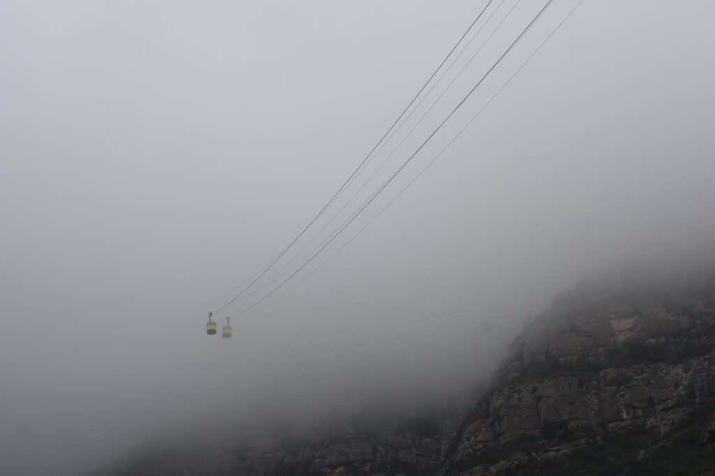 Two Montserrat cable cars crossing above the cliffs during a foggy morning