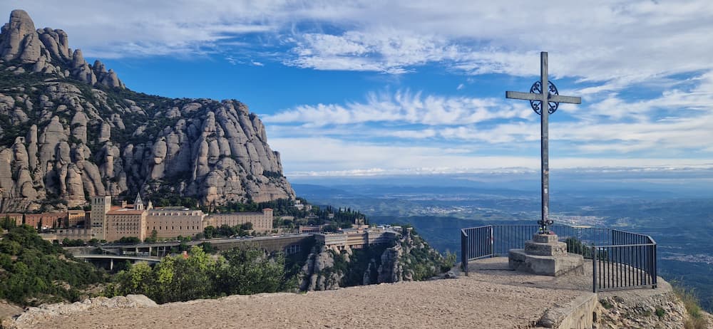 Montserrat things to do: the Creu de Sant Miquel cross with the monastery and the rock pillars behind