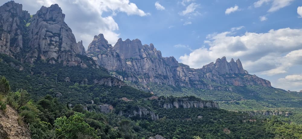 Panoramic view of Montserrat mountain in spring with green forest and cloudy blue sky