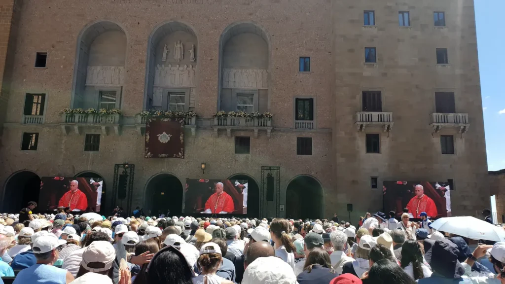 Pilgrims in Plaça de Santa Maria watching Pope Leo XIV on giant screens during the rosary at Montserrat