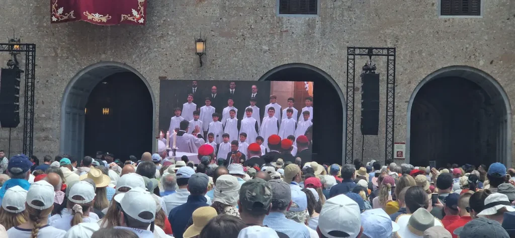 Montserrat boys choir on the big screen singing for Pope Leo XIV, with the monastery square packed with pilgrims, June 2026